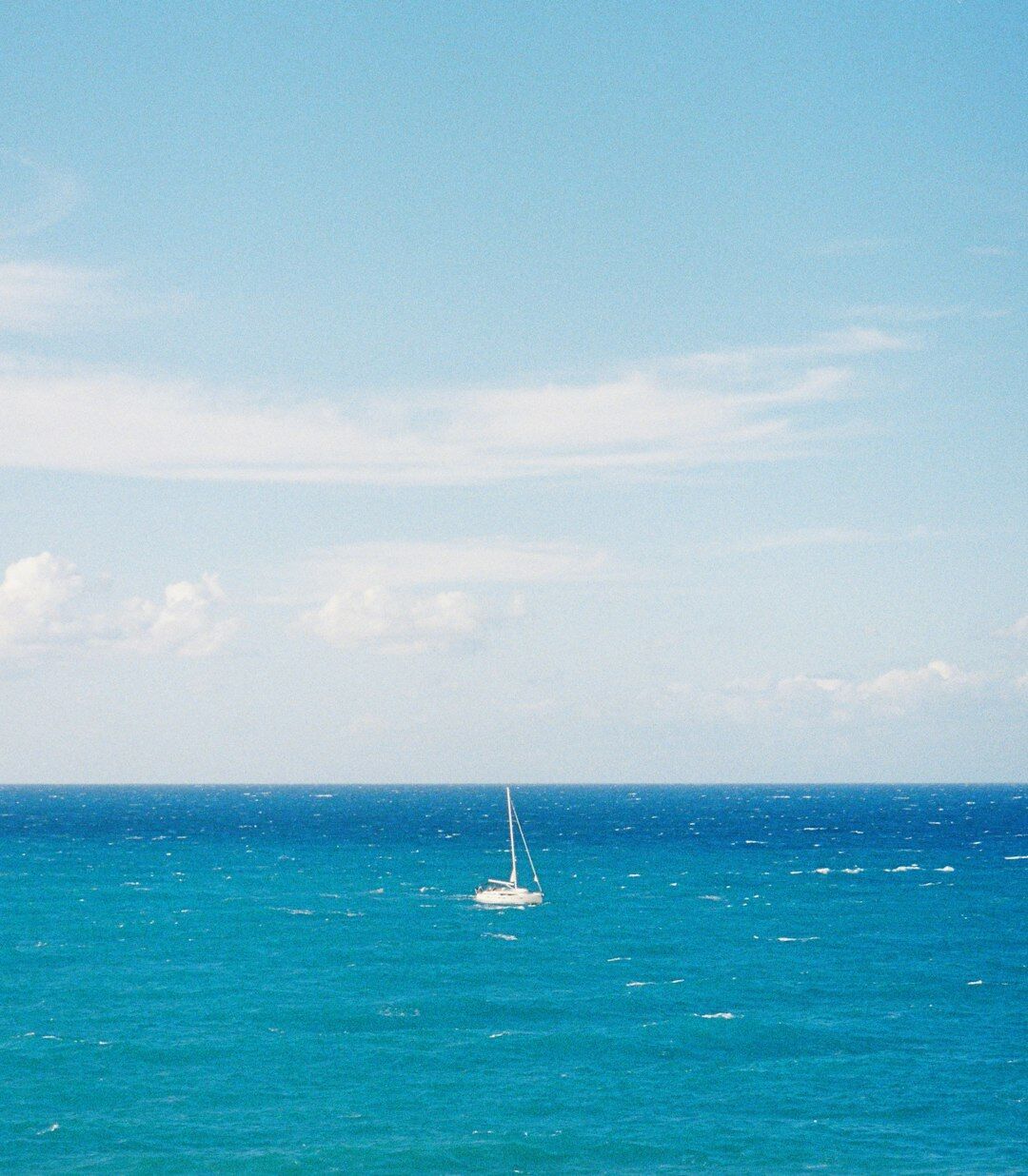Minimalist photograph of lone sailboat on calm blue sea